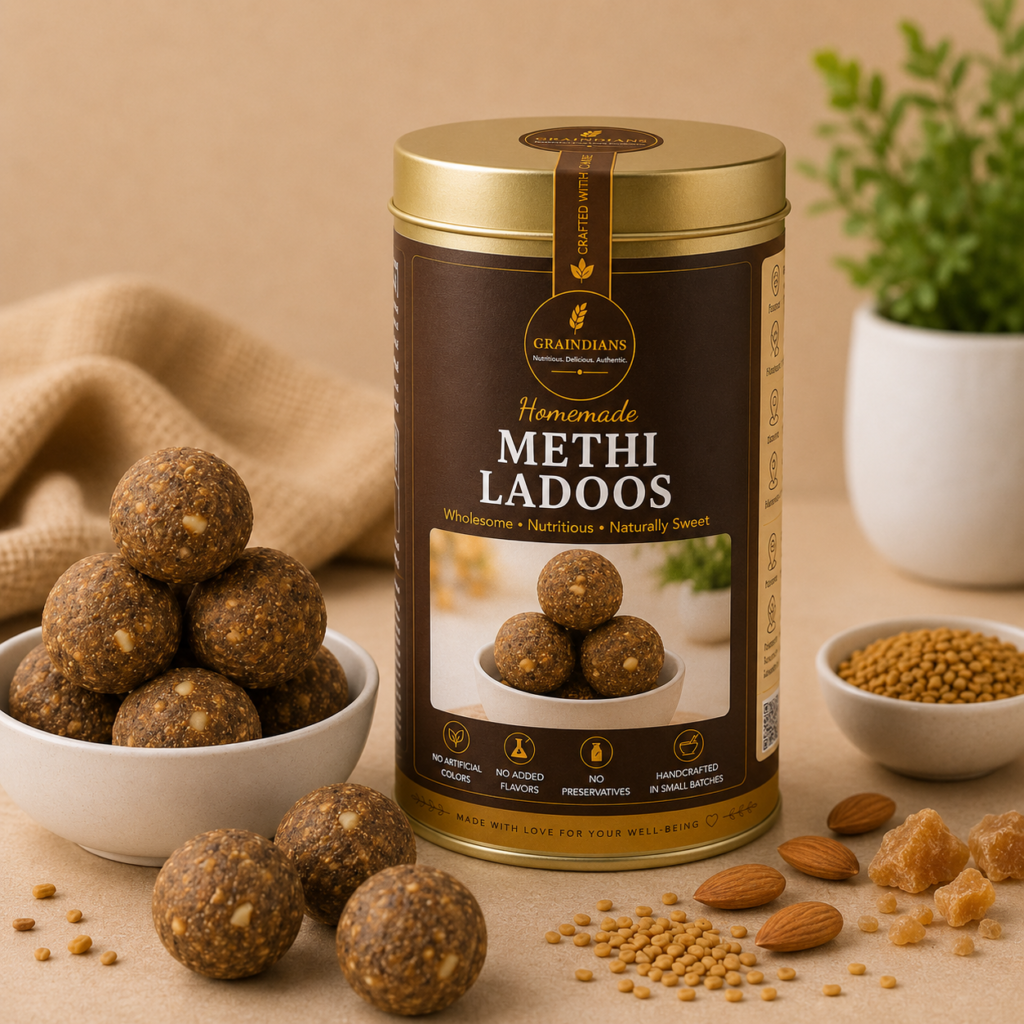 Graindians Homemade Methi Ladoos in a premium gift tin with fresh fenugreek ladoos, methi seeds, almonds and jaggery displayed on a warm beige background.